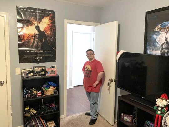 Jonathan Jarvis stands in the doorway of his room, which he calls the bat cave. Jarvis, who has down syndrome, lives with a roommate who also has a disability. The pair live independently of their parents but need someone to check on them daily to ensure 